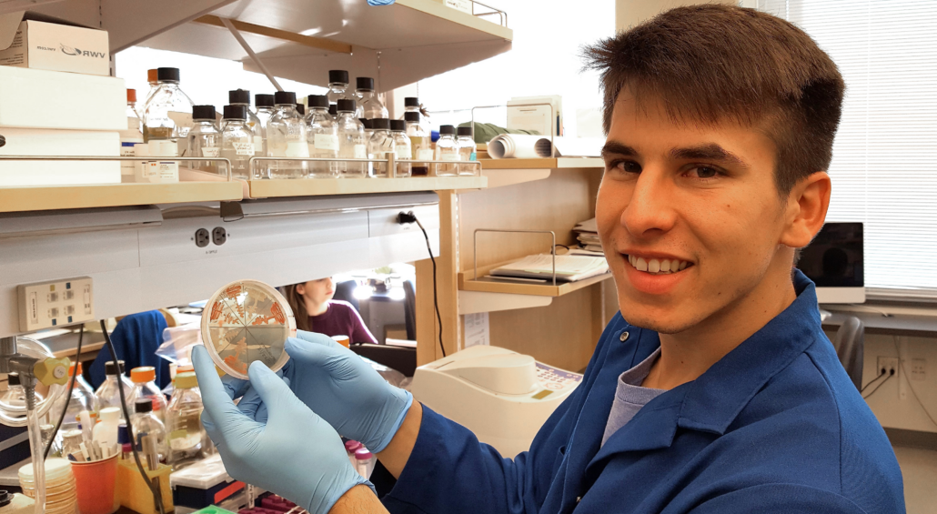 Student standing at a laboratory bench holding an agar plate.
